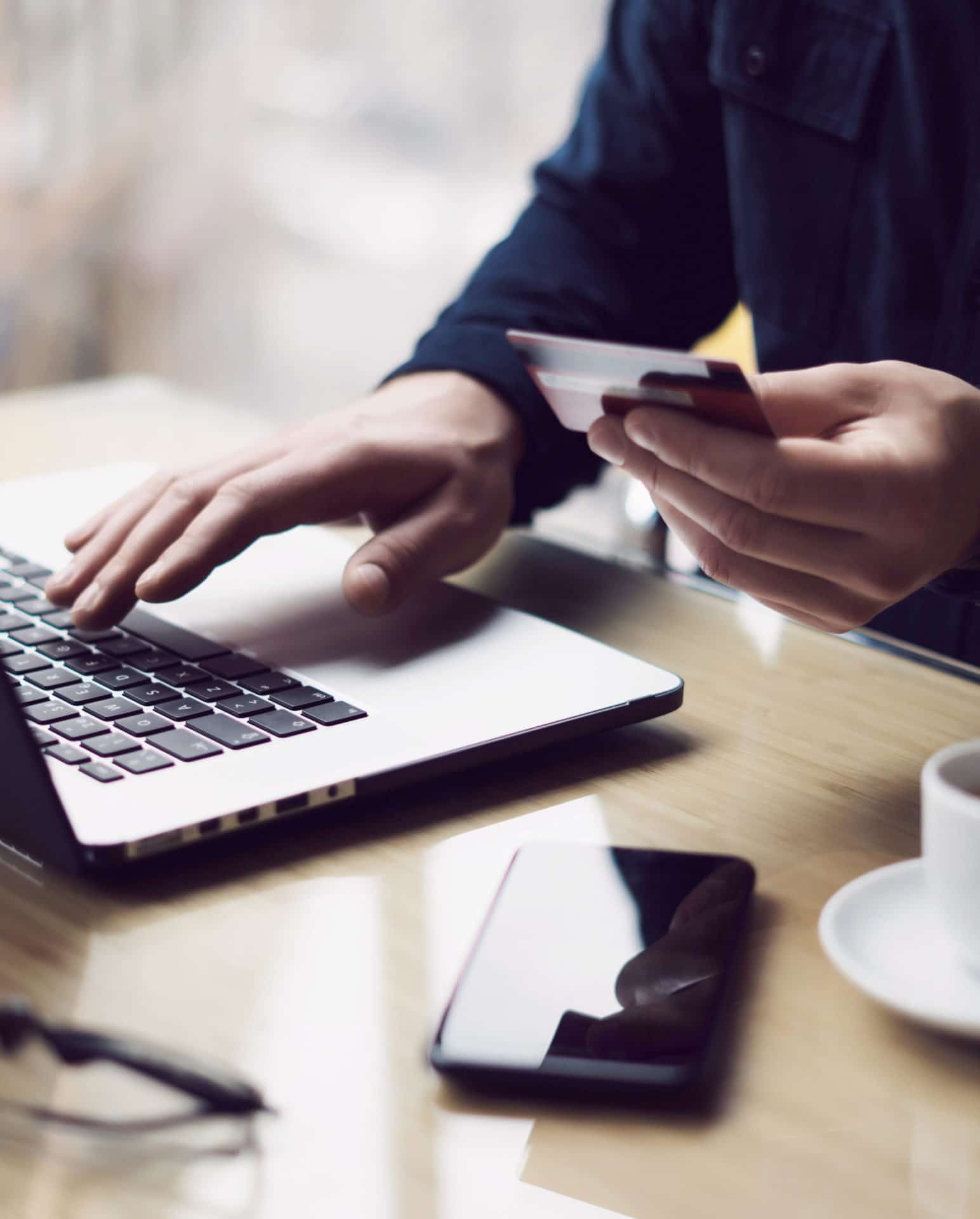 Businessman holding plastic credit card in hand and using laptop computer while sitting at the wooden table.Man making online shopping.Blurred background.Vertical.